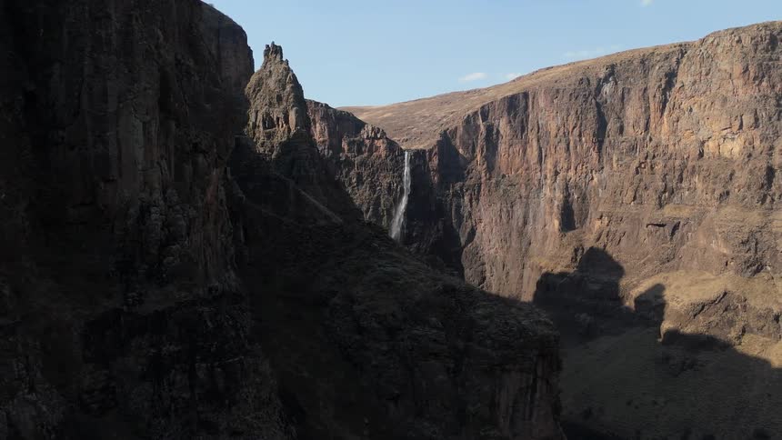 A waterfall cascading down a steep rocky cliff with barren cliffs and a clear blue sky