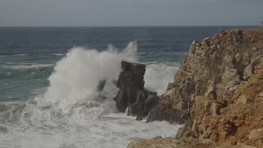Strong waves crashing and rising against the rocky coastline