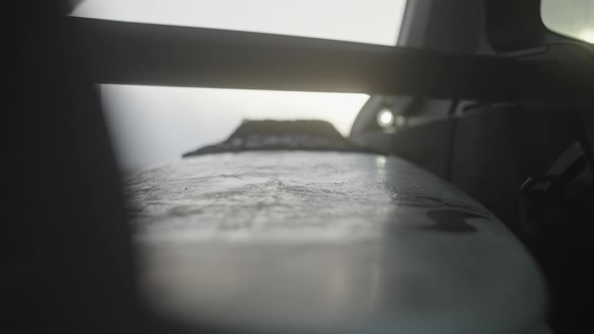 Close up of the hand of a person retrieving a surfboard from the truck of a car