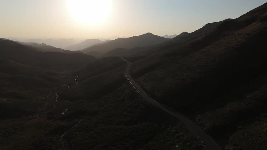 Silhouette of a highway winding through a mountain valley with the sun on the horizon