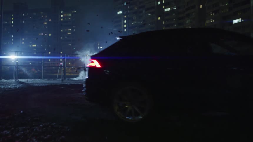 Car performing a stunt in the mud next to residential buildings in a city at night