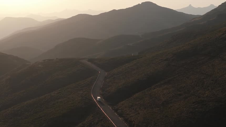 A car driving through winding road meandering through rolling hills with a hazy golden light