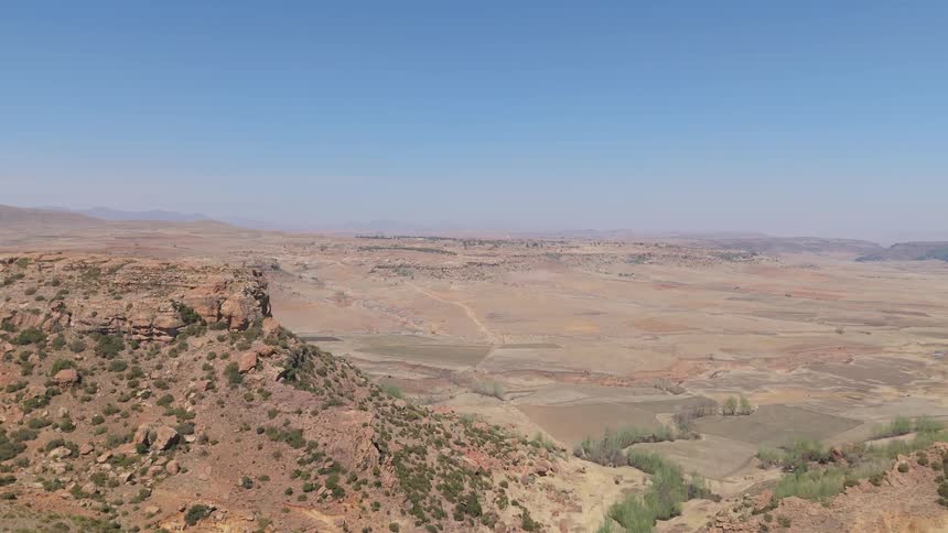 A vast dry desert landscape with rocky cliffs and a clear blue sky