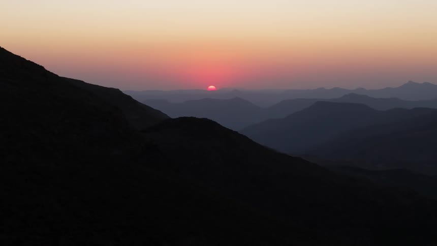 Fog hangs over the mountains as the sun sets in a colorful hazy sky