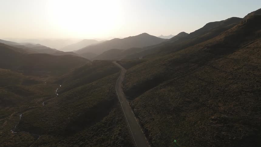 Aerial landscape of a highway winding through mountains with the sun on the horizon
