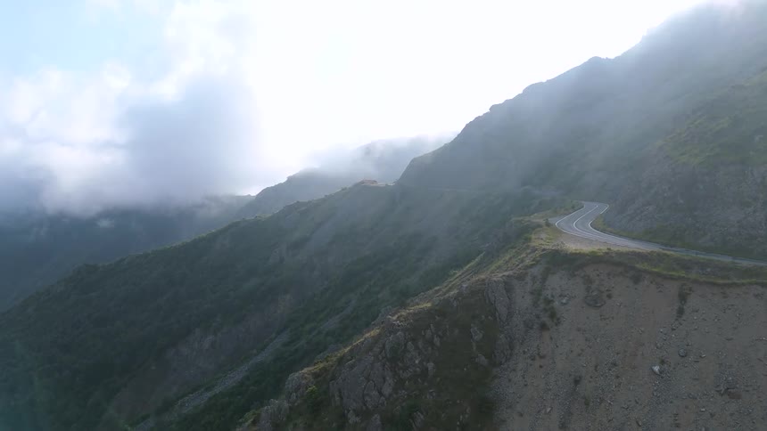 Winding road stretches along a mountainous landscape covered by low clouds