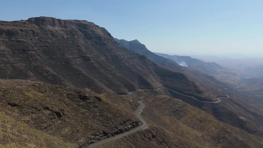 A winding road cutting through a rugged mountainous landscape with clear skies above and deep valleys below