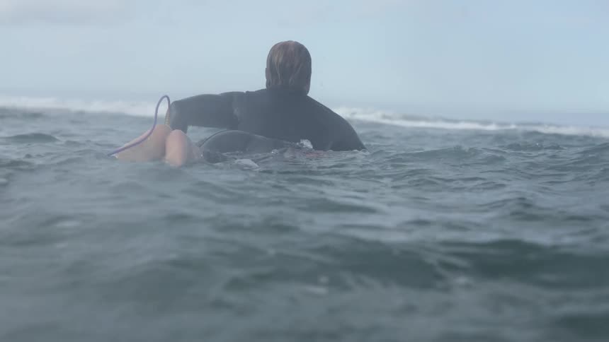 A male surfer paddles on a surfboard in the ocean