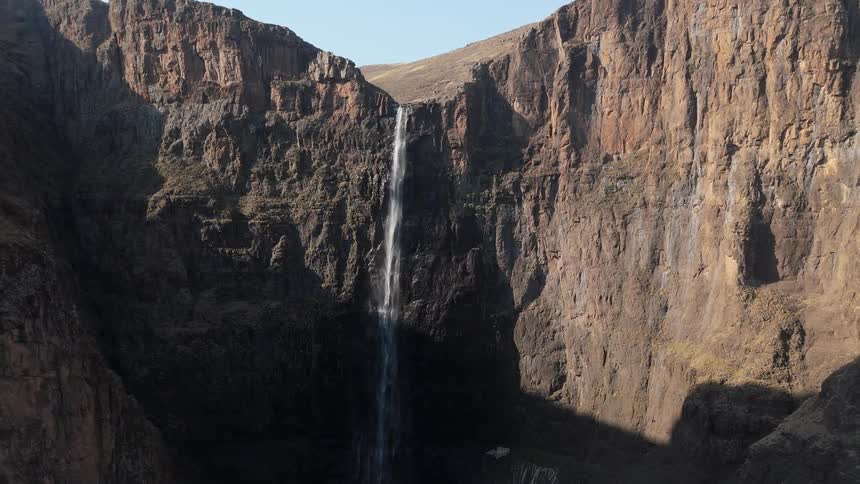 A tall thin waterfall pours over a cliff in a mountainous area