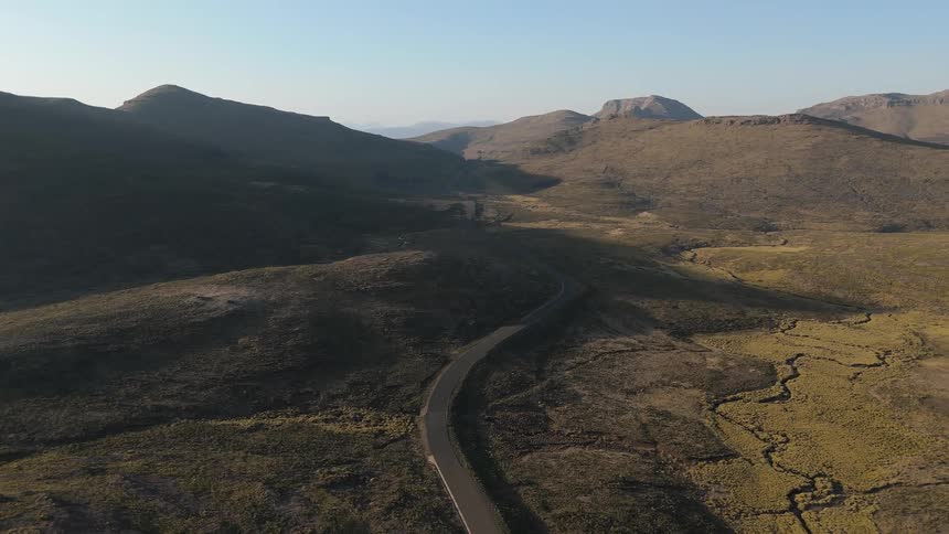 Aerial shot of a long highway running through a mountain valley on a blue sky day