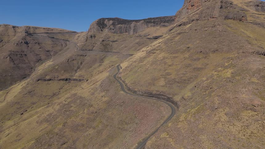 Aerial view of a winding road cutting through a barren mountainous landscape with steep cliffs and sparse vegetation