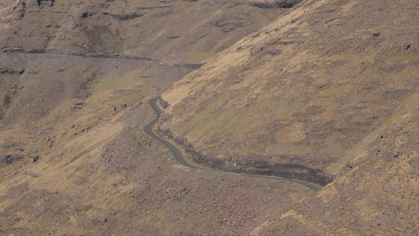 A winding road cutting through a barren hilly landscape with no visible vegetation