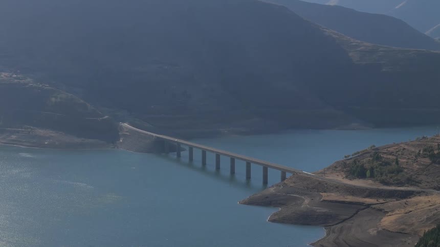 Aerial view of a long bridge crossing a water reservoir surrounded by mountains