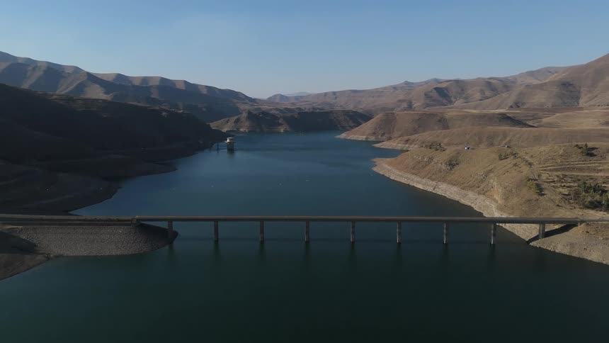 Aerial view of a long bridge above a reservoir with mountains around