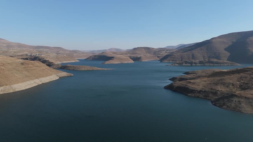 A large lake in a mountainous region with rugged sparsely vegetated hills and a clear sky