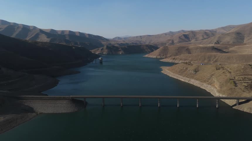 Aerial view of a dam surrounded by mountains with a water reservoir behind it
