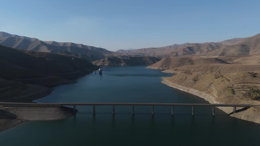 Large dam with a reservoir in the background surrounded by arid mountainous terrain