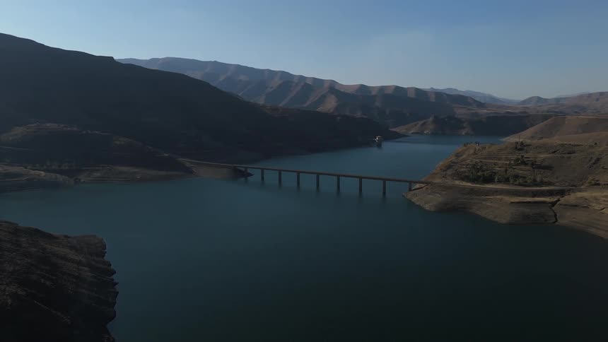 Aerial view of a bridge spanning over a calm body of water with mountainous terrain in the background