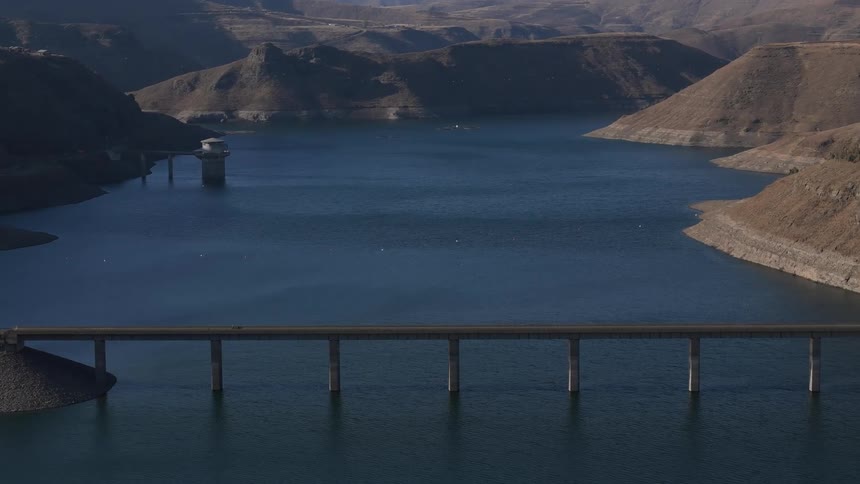 A bridge spans across a body of water with hills visible in the background
