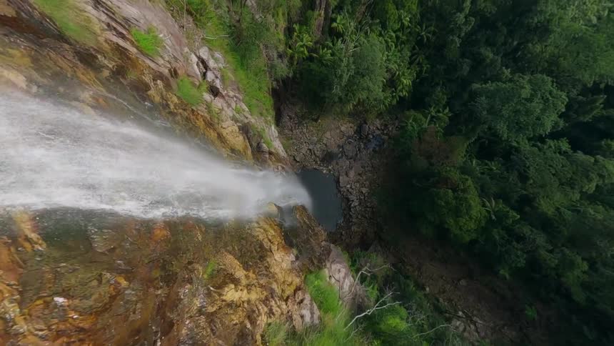 A tall thin waterfall pours over a rock face into a small pool in a jungle