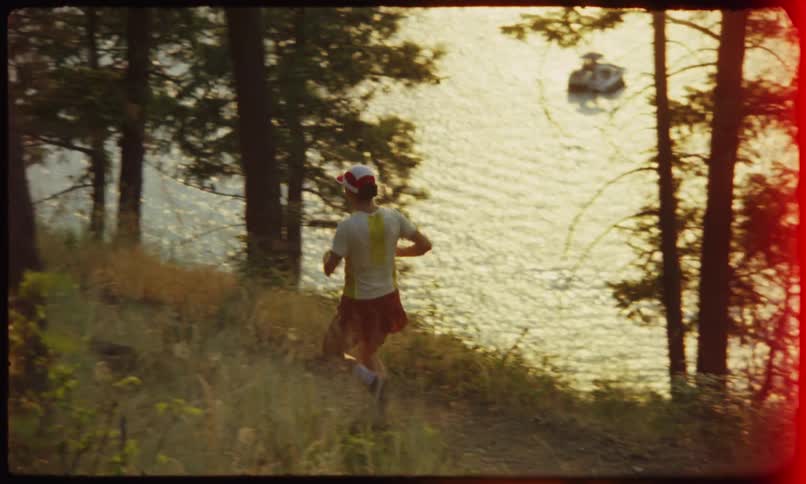 A person is running with his back turned on a dirt path next to some trees and on the right side there is a sea
