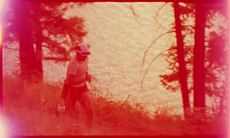 A woman in a cap is running on a grassy path with some trees behind and in the background there is a sea