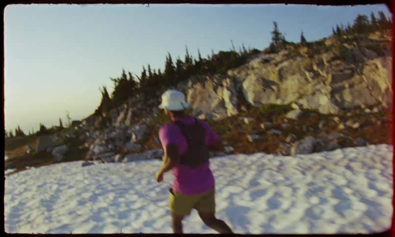 Man from behind wearing a purple tshirt and a white cap running on a snowcovered terrain with trees