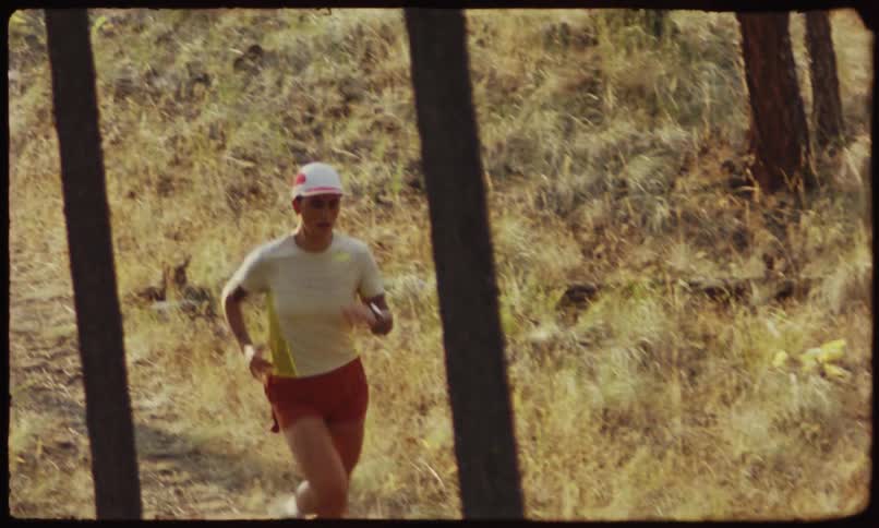 A woman in shorts and a cap jogs through a forest