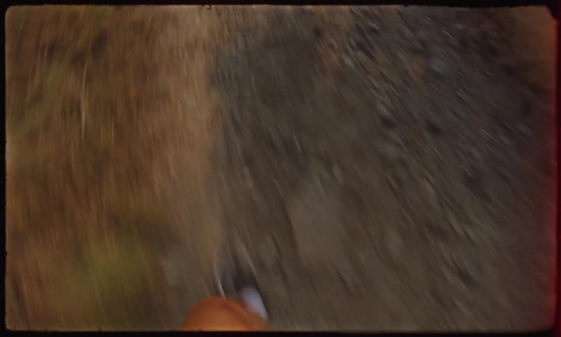 The feet of a person running on a dirt path and then looks ahead and where there is a landscape of a lake between mountains