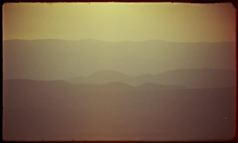 Silhouette landscape of mountains against a golden sky with sun flare
