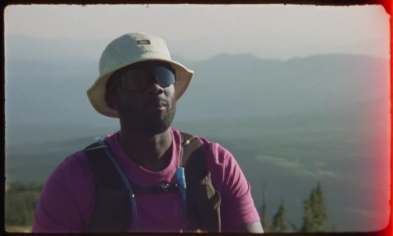 Male backpacker takes a break in a field overlooking a foggy valley in order to eat
