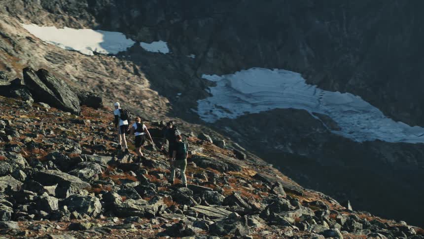 Backpackers hike up a boulder strewn slope overlooking a partially shadowed valley