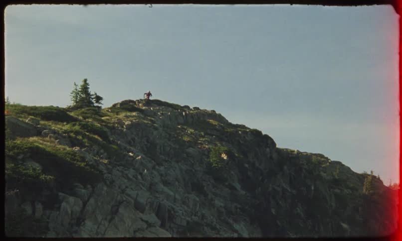 A person is running on the peak of a stone mountain with some vegetation on top