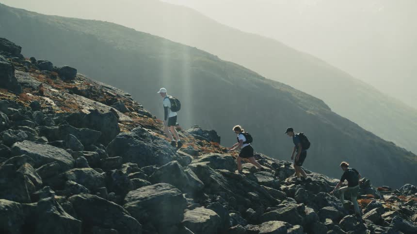 Backpackers hike up a steep boulder strewn mountain side on a foggy day
