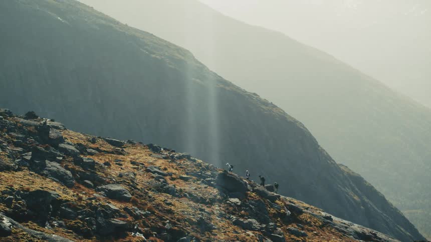 Sun glares through the haze onto backpackers hiking up a mountain slope