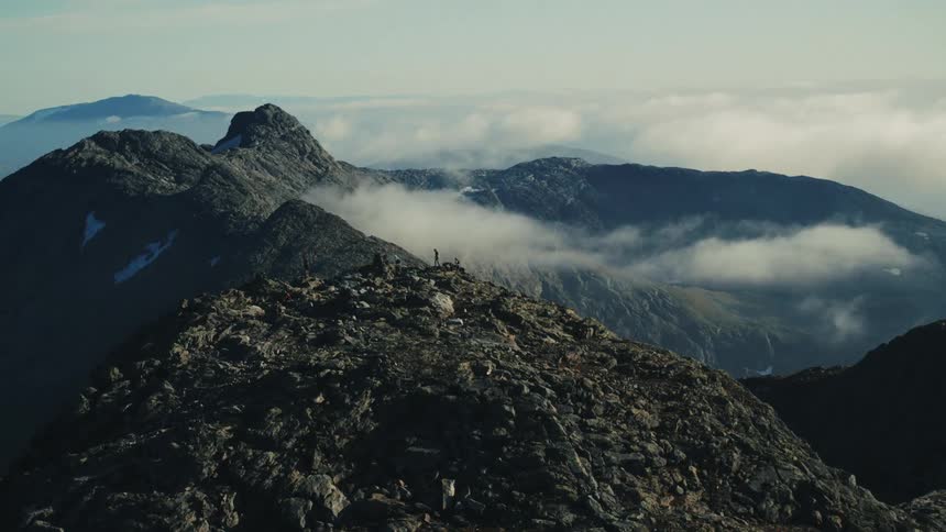 Four hikers climb a rocky mountain near a large range of mountains
