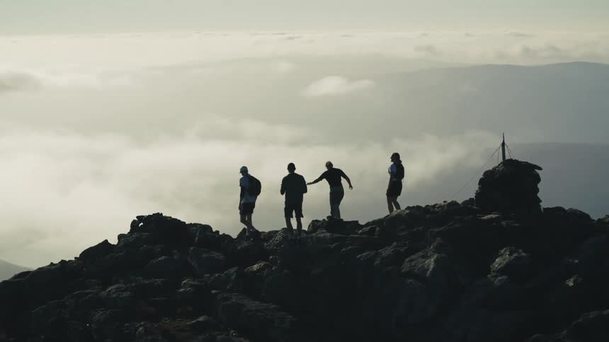 A group of four people on top of a mountain of rocks are celebrating by waving their arms