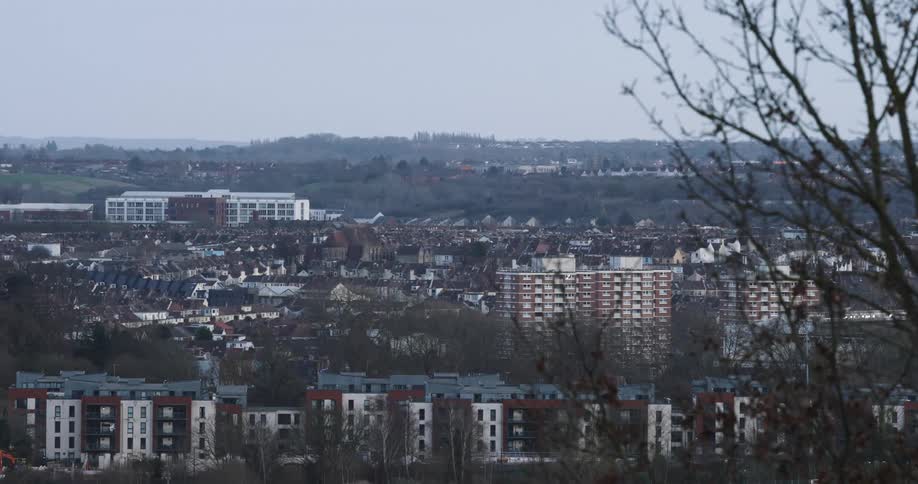 A view of a city with several mediumsized buildings and some houses in the background on a day with a white sky