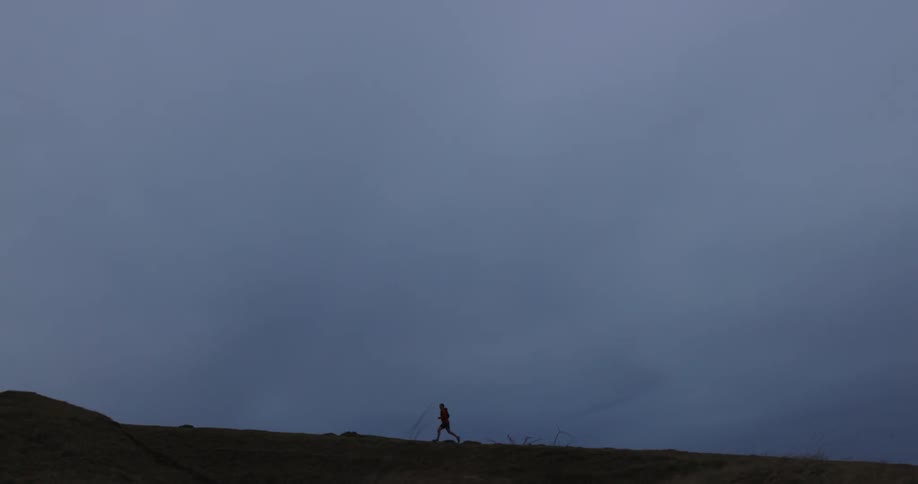 A female jogger runs along a ridge on a grassy plain
