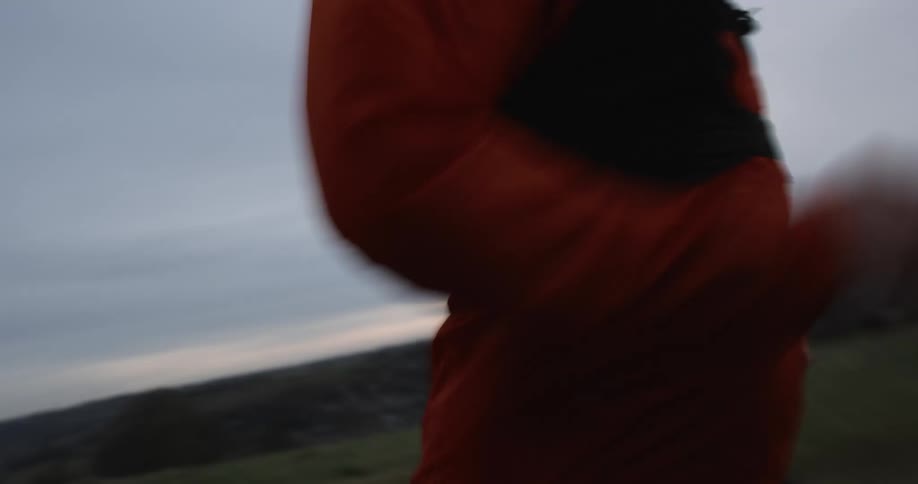 A runner in red clothing runs across a field at dusk