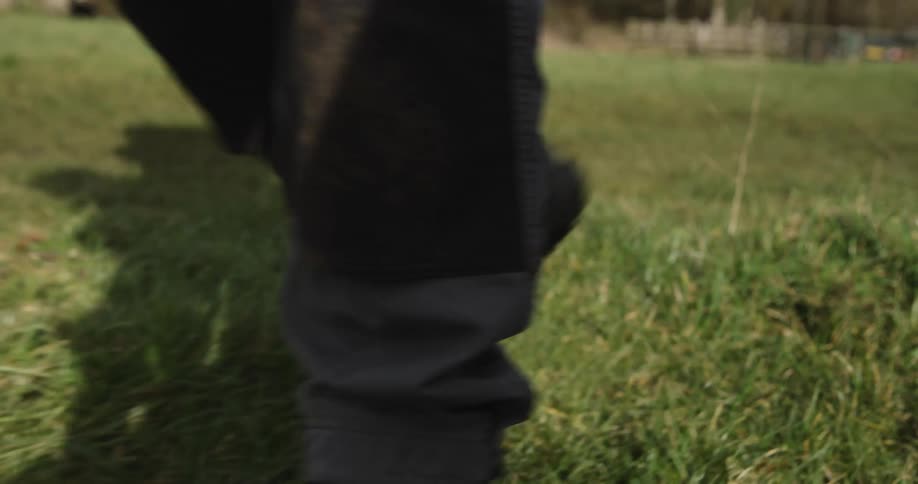 A pair of feet in dark shoes walk across a field of tall grass