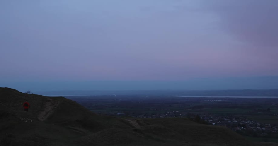 A lone figure runs along a hillside overlooking an expansive twilight landscape