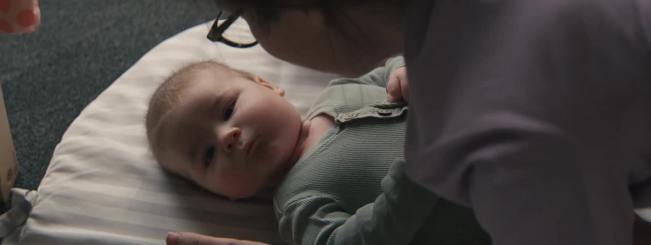 An adult with glasses holds a baby close to their face while the baby spits up a bit