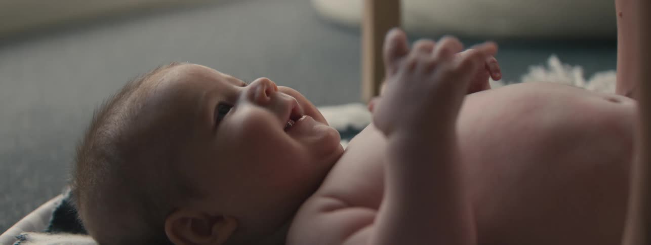 An adult hand touching the nose of an infant laying on its back on a rug