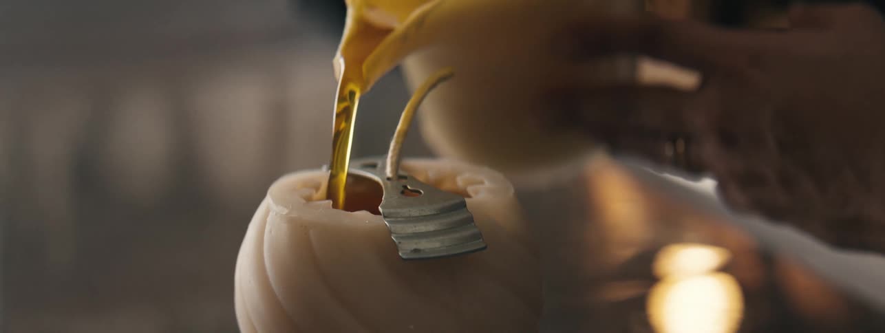 Woman pours melted wax into the middle of a solid wax candle exterior to attach the wick