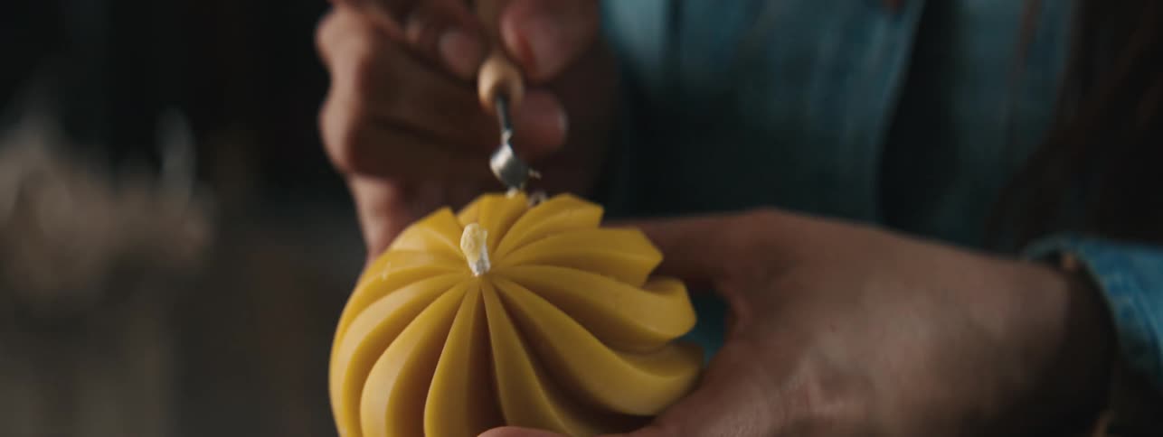 Hands of a craftswoman working on a yellow spherical object with tweezers