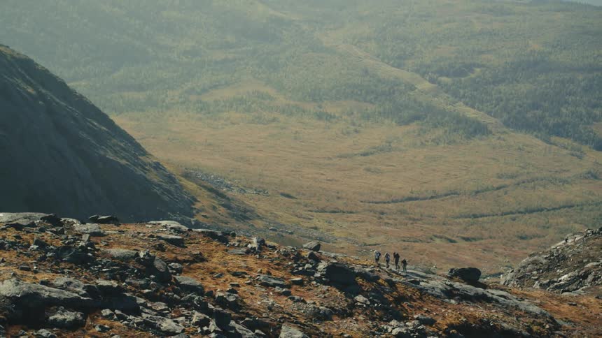 Four hikers move across the top of a mountain with a giant partially forested valley below them