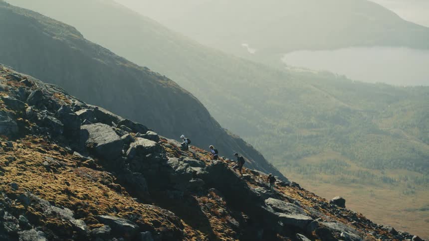Aerial view of a group of people climbing a mountain in a valley with the sea in the background