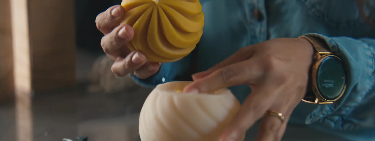 Pair of hands of a craftswoman removing a mold from a yellow spherical candle