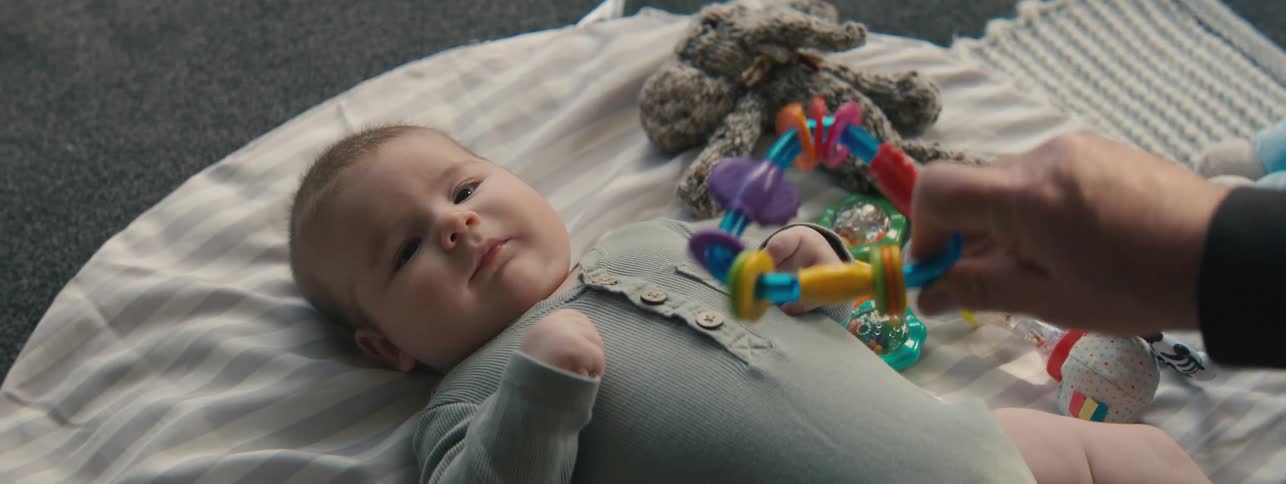 Father with toy interacting with his baby son lying down